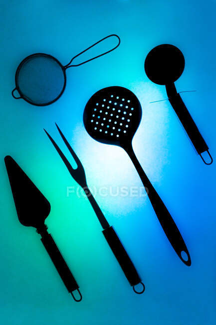 Вид сверху композиция разнообразных кухонных инструментов, расположенных на освещенной синей стеклянной поверхности — стоковое фото
