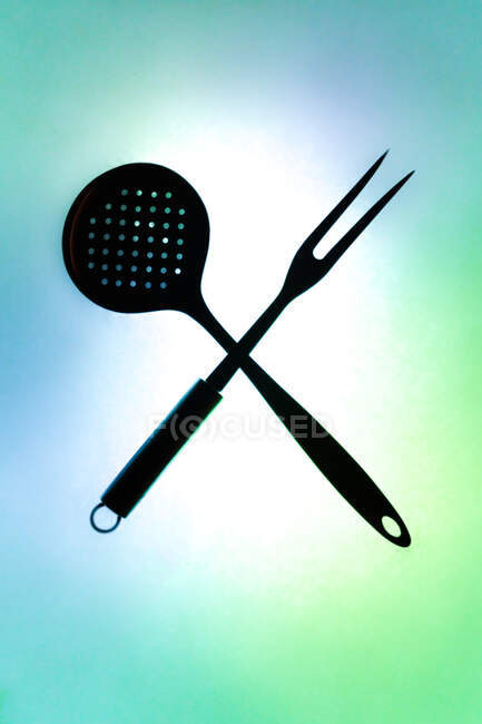 Composition vue de dessus avec écumoire de cuisine et fourchette de cuisson disposées en forme de X sur fond vert éclairé — Photo de stock