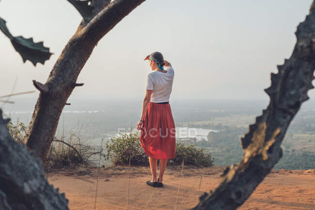 Rückenansicht einer Frau in lässigem T-Shirt und Rock, die auf einem sandigen Hügel steht und ihr Gesicht bedeckt, während sie den Sonnenuntergang genießt und durch Sri Lanka reist — Stockfoto