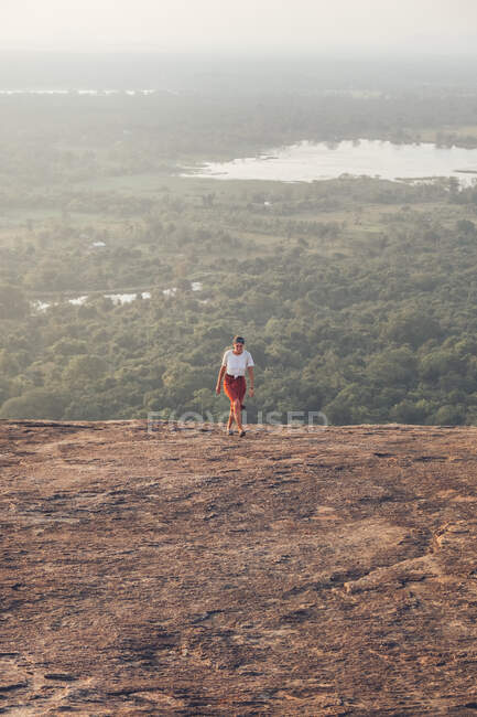 D'en haut de voyager femelle en vêtements décontractés courant vers le haut sur fond de vallée avec forêt et lac pendant les vacances d'été à Sigiriya — Photo de stock