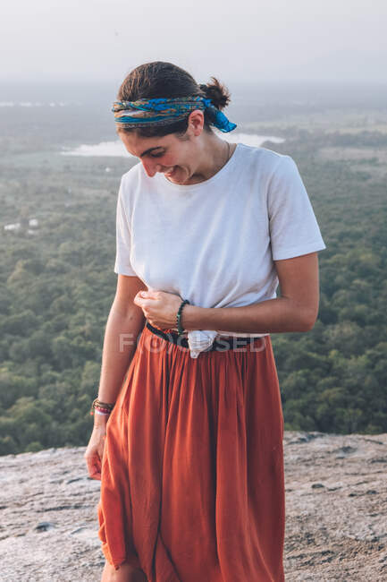 Serena mulher viajando em roupas casuais e bandana admirando paisagem cênica durante as férias em Sigiriya enquanto estava de pé em volta iluminado e olhando para longe — Fotografia de Stock
