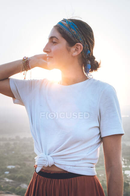 Vista lateral da mulher viajante serena em roupas casuais e bandana admirando a paisagem cênica durante as férias em Sigiriya enquanto estava de pé na parte de trás iluminado e olhando para longe — Fotografia de Stock