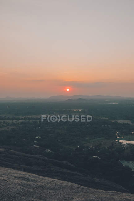 Desde arriba de majestuosa vista del sol y siluetas de picos de montaña durante la puesta del sol en Sigiriya - foto de stock