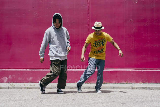 Dos jóvenes bailando cerca de una pared rosa en la calle - foto de stock