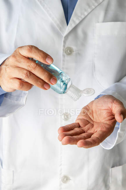 Terapeuta masculino en bata médica manos desinfectantes con antiséptico - foto de stock