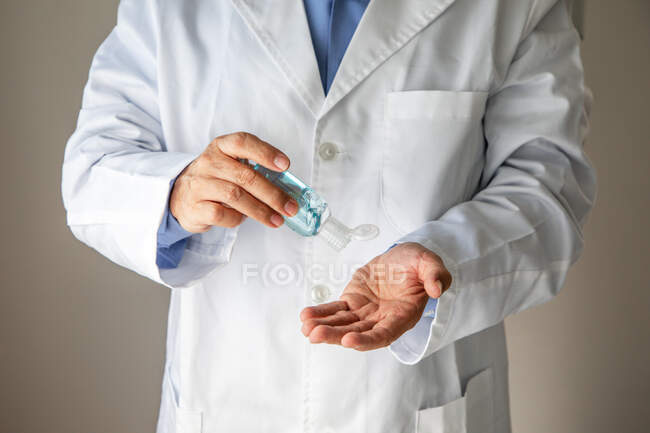 Мужской терапевт в медицинском халате дезинфицирует руки антисептиком — стоковое фото