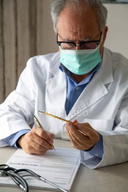 Medico di sesso maschile con maschera protettiva che scrive su carta e guarda il termometro — Foto stock