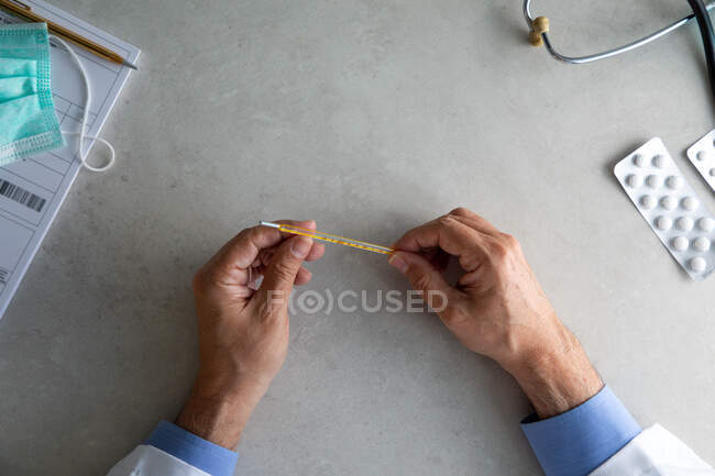 Male doctor hand holding thermometer at working desk — Stock Photo
