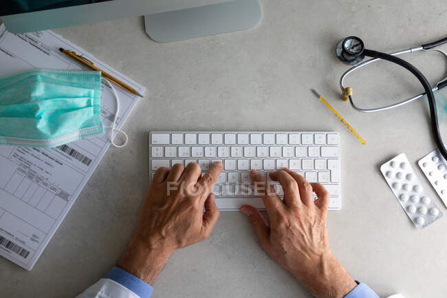 Мужские руки врача, печатающие на клавиатуре компьютера за рабочим столом — стоковое фото