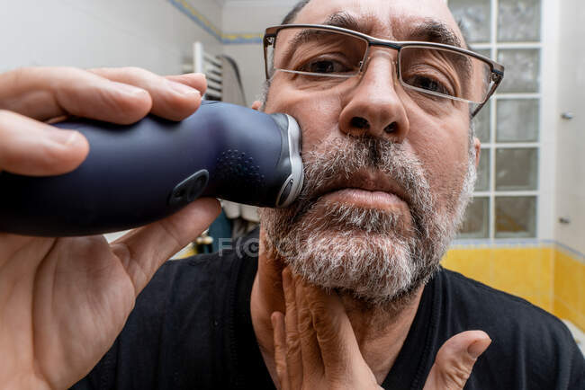 Hombre maduro afeitándose con afeitadora eléctrica - foto de stock