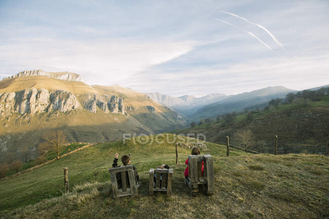 Bambini in abiti casual seduti su panchine di legno sulla collina verde remota e godendo della vista durante la visita in Spagna — Foto stock
