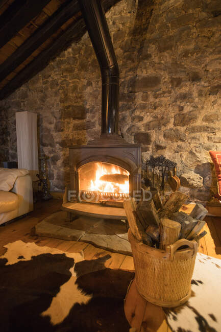 Living room interior with cozy carpets and burning flame in fireplace against stone wall in countryside house — Stock Photo