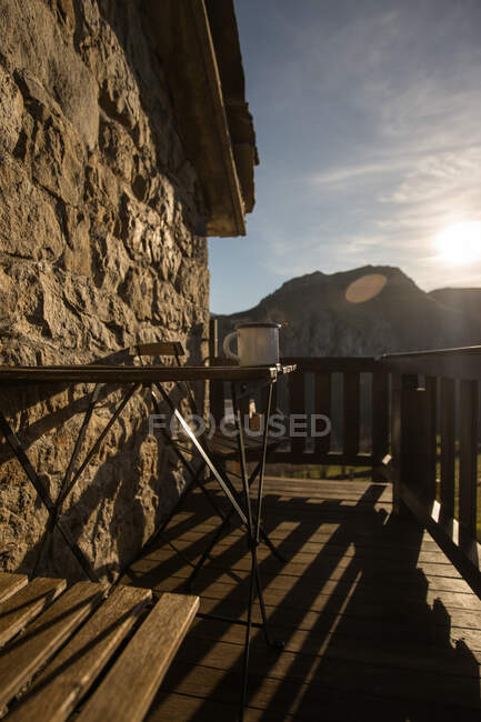 Dampfender weißer Becher mit frischem Heißgetränk auf Holztisch auf sonniger Terrasse des Steinhauses im sonnigen Kantabrien — Stockfoto