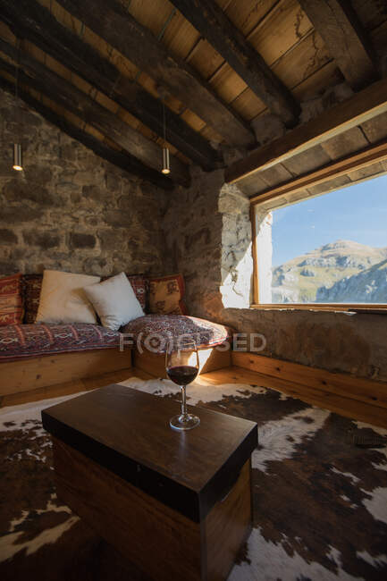 Innenraum eines gemütlichen Landhauses in Kantabrien mit gemütlicher Couch mit bunten Kissen und einem Glas Rotwein auf dem Tisch vor dem großen Fenster — Stockfoto