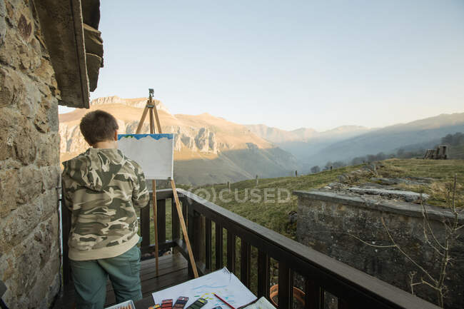 Anonyme garçon peinture à chevalet sur terrasse ensoleillée dans la campagne de l'Espagne — Photo de stock