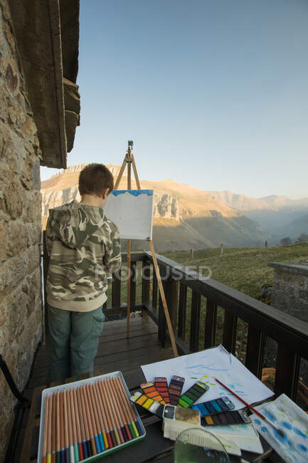 Anonyme garçon peinture à chevalet sur terrasse ensoleillée dans la campagne de l'Espagne — Photo de stock