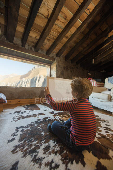 Хлопчик сидить на підлозі на затишному килимі і малює з кольоровими олівцями в скетчері холодної затишної вітальні кам'яного будинку в Кантабрії. — стокове фото