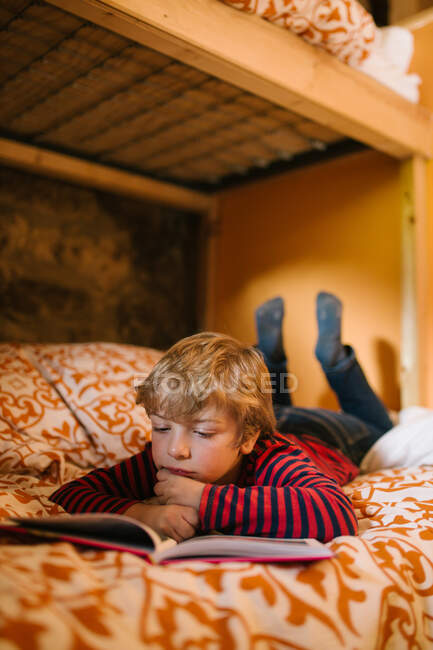 Мечтательный ребенок в повседневной одежде лежит на уютной кровати и наслаждается интересной сказкой в книге рассказов для детей — стоковое фото
