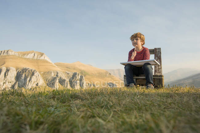 Entzückendes Kind sitzt auf Holzbank und malt am Wochenende auf Leinwand vor dem Hintergrund der herrlichen Berglandschaft — Stockfoto