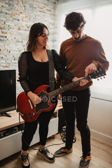 Мужчина учит женщину играть на гитаре дома — стоковое фото