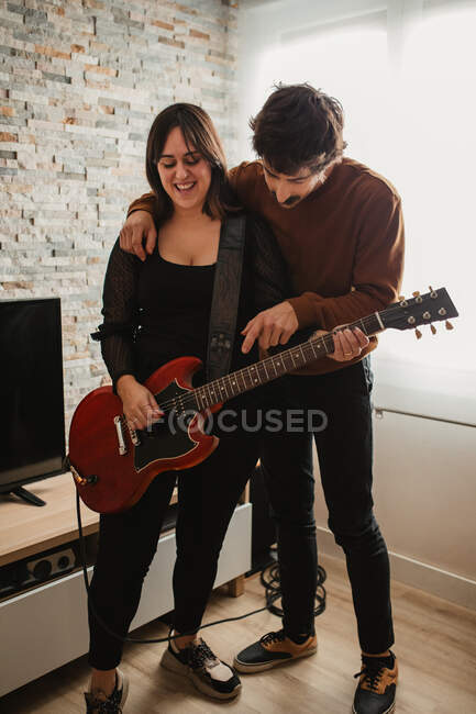 Homem ensinando mulher a tocar guitarra em casa — Fotografia de Stock