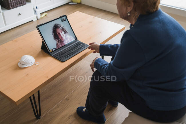 Vue de dessus de la femme âgée assise à la table et ayant une conversation en ligne via un ordinateur portable avec sa fille tout en restant à la maison pendant la pandémie de coronavirus — Photo de stock