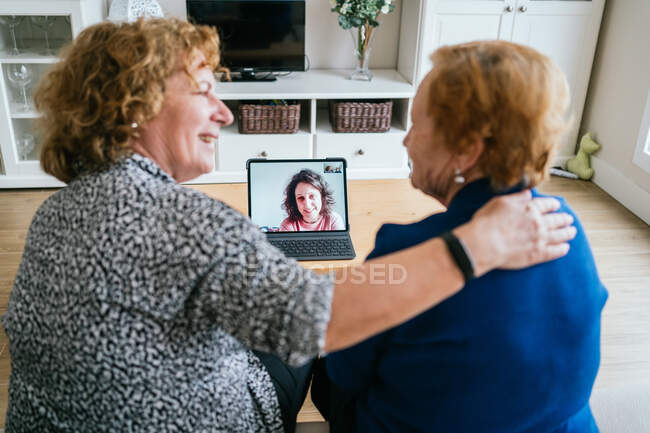 Vista posteriore di donne anziane allegre che chattano con un amico durante la riunione video online via computer portatile mentre rimangono a casa durante l'isolamento coronavirus — Foto stock