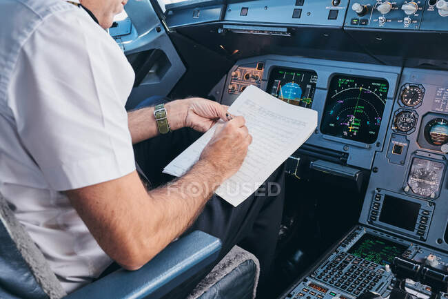 Vista lateral do aviador macho de colheita sentado no cockpit e preenchendo o documento enquanto se prepara para o voo em aeronaves modernas — Fotografia de Stock