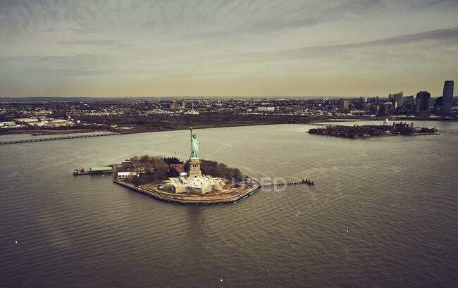 Вид с воздуха на остров Свободы и Статую Свободы в гавани Нью-Йорка на фоне городского пейзажа и облачного неба — стоковое фото