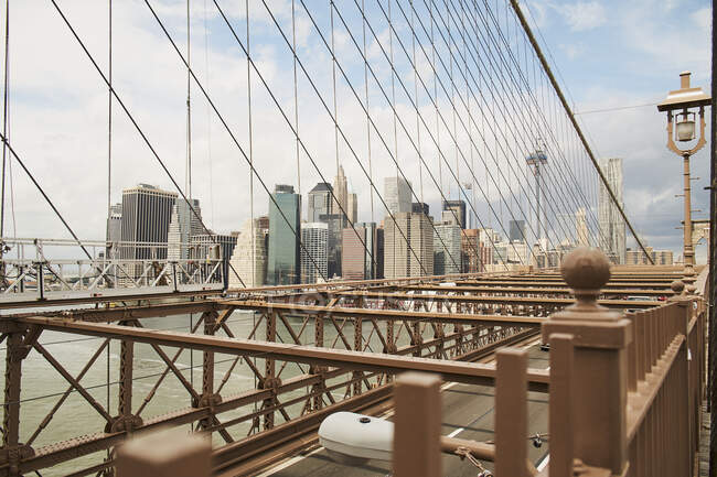 Des gratte-ciel contemporains de New York vus à travers des câbles du pont de Brooklyn contre un ciel nuageux bleu — Photo de stock