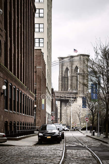 Ferrovia passando pela rua de paralelepípedos com carros estacionados perto de edifícios altos no distrito da cidade velha, em Nova York, no dia nublado da primavera — Fotografia de Stock