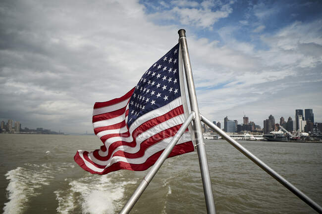 Національний прапор США махаючи на полюсі плавучого судна проти хмарного неба біля берегів Нью - Йорка. — стокове фото