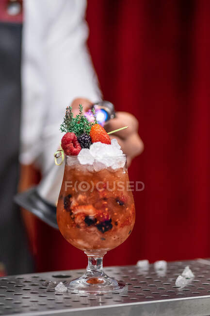 Tiro cortado de barman usando queimador acabamento de coquetel de frutas com gelo e ervas frescas no balcão do bar — Fotografia de Stock