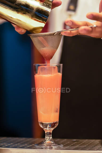 Скручений знімок бармена, що тримає сито і заливає освіжаючий коктейль від шейкера в склянку — стокове фото