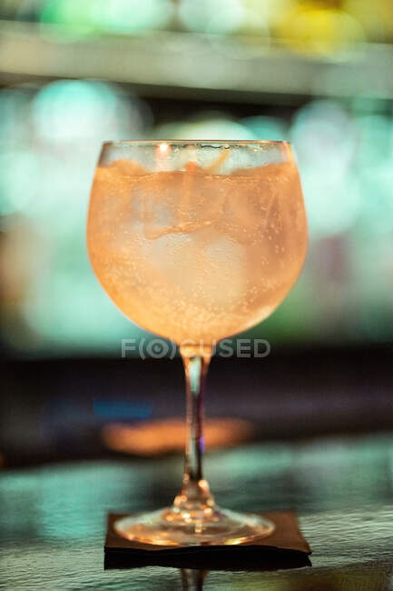 Alcohol tonic cocktail with ice cubes against blurred neon background — Stock Photo