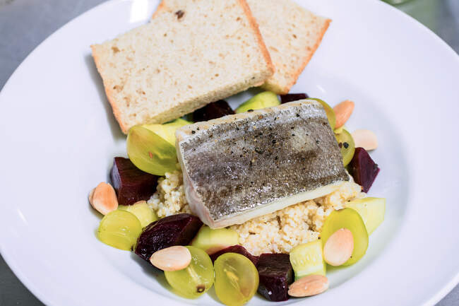 Poisson servi avec salade de quinoa au raisin et betterave sur assiette blanche avec tranches de pain — Photo de stock
