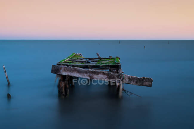 Tiro de larga exposición con ondas borrosas, musgoso muelle de madera vieja en el mar con el cielo del amanecer - foto de stock