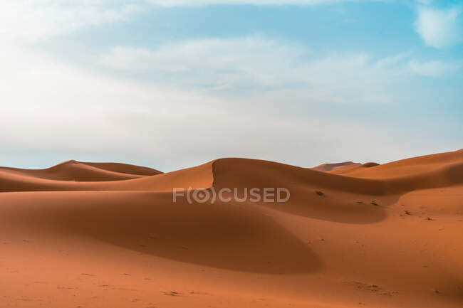 Paysage désertique minimaliste avec des dunes de sable sous un ciel nuageux bleu — Photo de stock