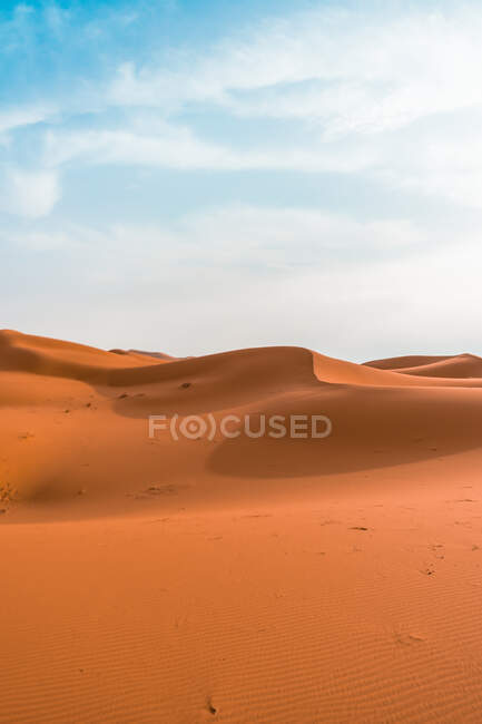 Paesaggio desertico minimalista con dune sabbiose sotto il cielo nuvoloso blu — Foto stock