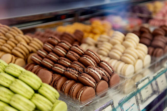 Muitos macaroons saborosos coloridos de cores diferentes com vários recheios e gostos sortidos por cores em recipientes em pé na janela de exibição na pastelaria — Fotografia de Stock