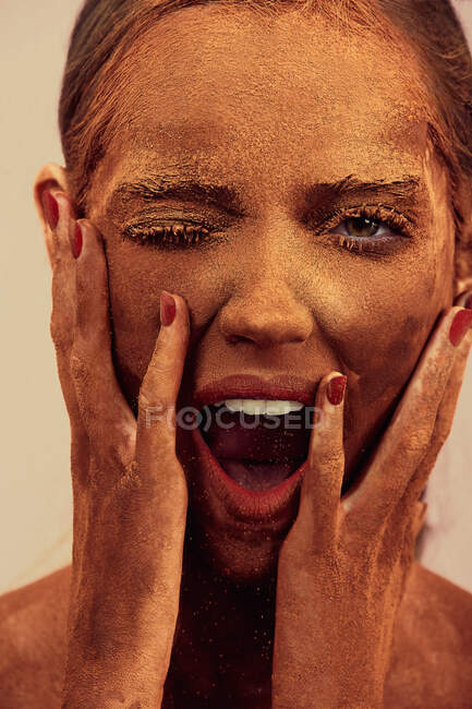 Attractive female model with chocolate on skin touching face and yelling at camera with closed eye — Stock Photo