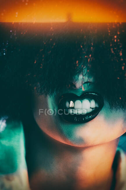 Обрезание женской модели в синтетическом парике и с черной помадой, показывающей зубы под ярким светом — стоковое фото