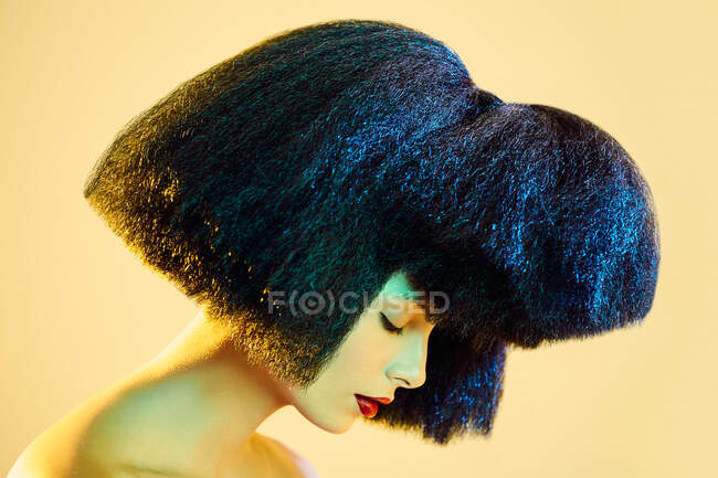 Crop female model in synthetic wig and with black lipstick showing teeth under colorful light — Stock Photo