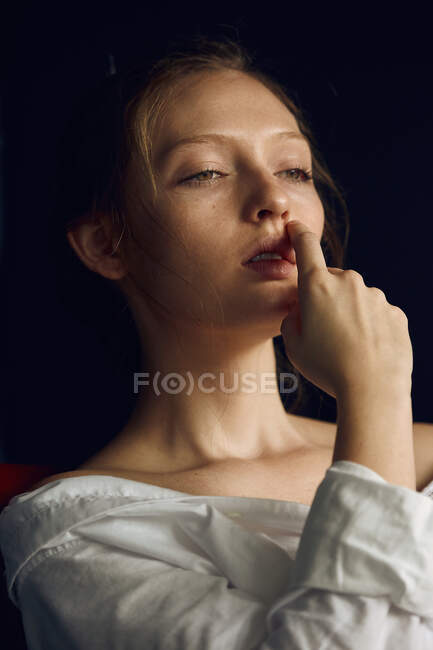 Приваблива молода жіноча модель в білій сорочці з голим плечем, що торкається обличчя і дивиться в сторону — стокове фото