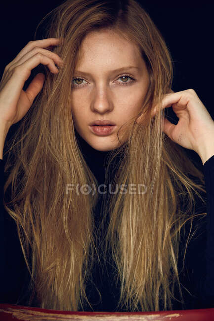 Schöne junge Frau blickt in die Kamera und zerzaust lange blonde Haare vor schwarzem Hintergrund — Stockfoto