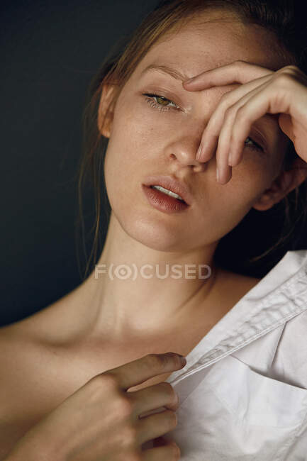 Attraktives junges Model in weißem Hemd mit nackter Schulter, das Gesicht berührt und wegschaut — Stockfoto