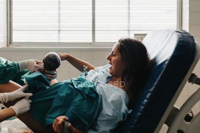 Напряженная женская рукоятка захвата и хрюканье от боли при рождении ребенка на медицинском стуле в современной больнице — стоковое фото