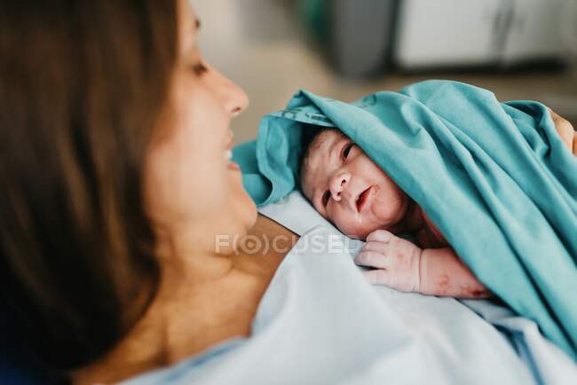 Hohe Winkel der fröhlichen erwachsenen Frau umarmt Neugeborenes mit Blut bedeckt nach der Geburt im Kreißsaal des modernen Krankenhauses — Stockfoto