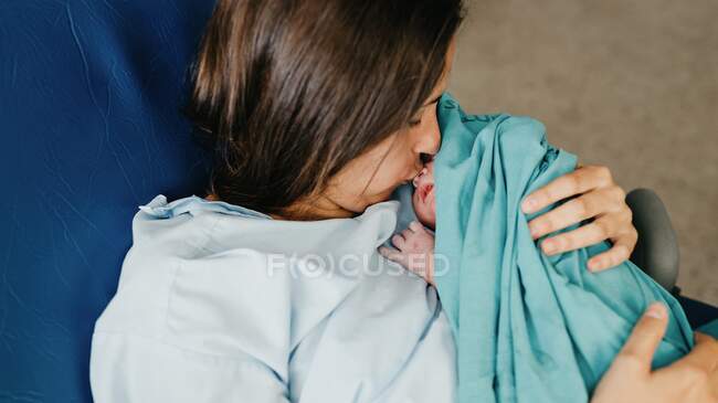 From above adult lady kissing infant in nose while sitting on chair in delivery room in modern hospital — Stock Photo