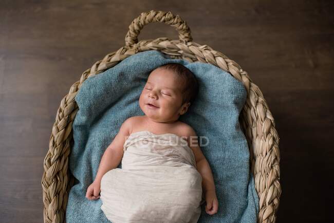Вид зверху новонародженої дитини, загорнутий в тканину, лежить на м'якій ковдрі і спить в плетеному кошику на підлозі вдома — стокове фото